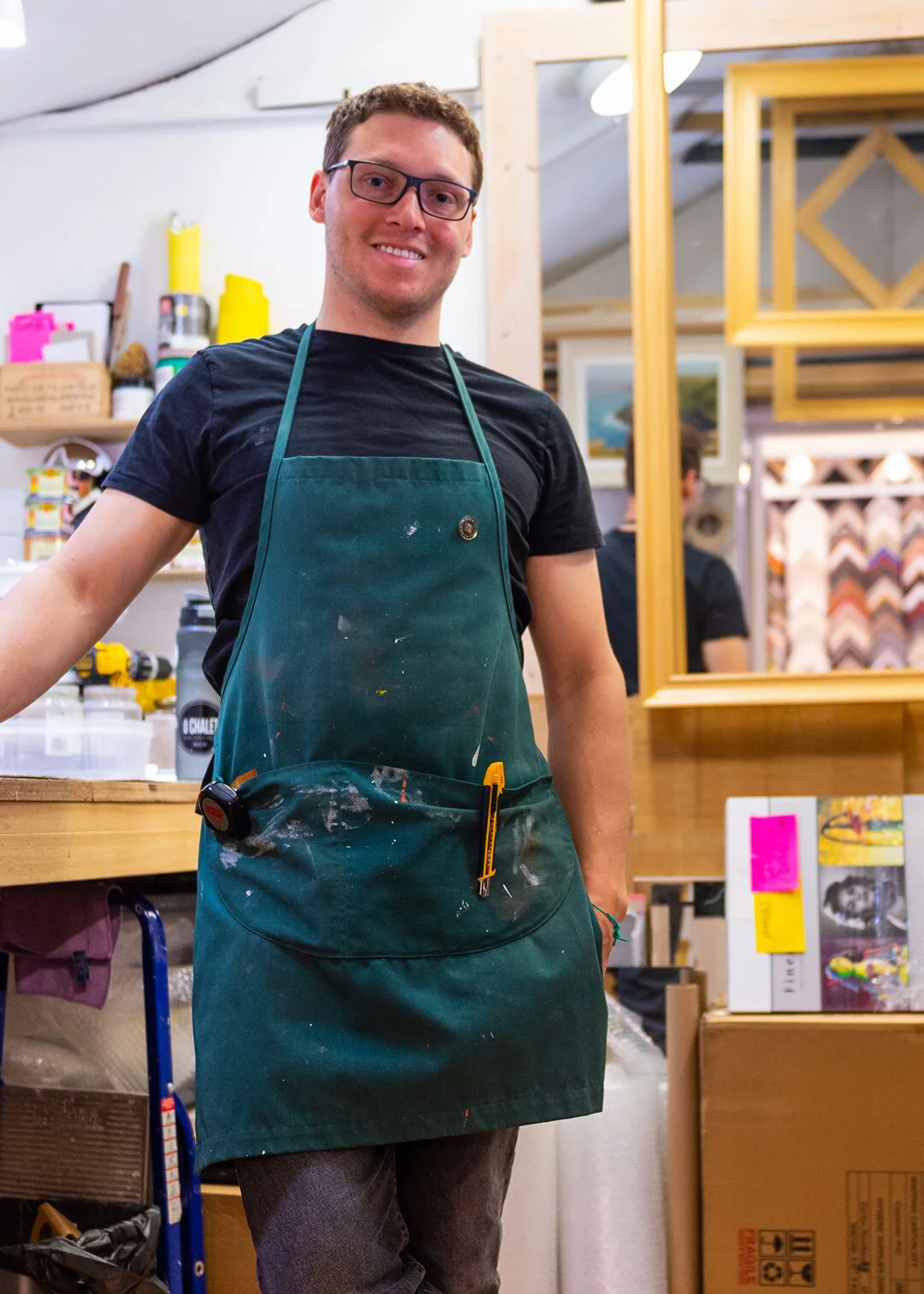 Elliot Dunford in a workshop apron beside gilt frames and moulding samples